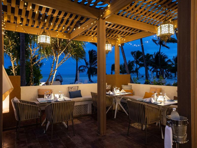 Terraza exterior acogedora de un hotel al atardecer con mesas y sillas bajo luz de faroles.