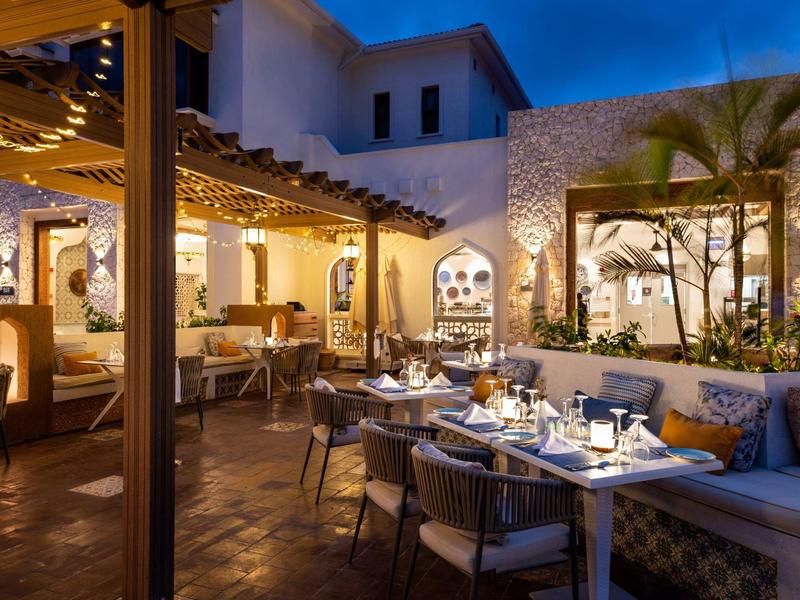 Acogedora terraza exterior de un hotel con mesas iluminadas y arquitectura mediterránea al anochecer.