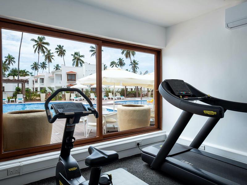 Gimnasio con cinta de correr y bicicleta estática con vista a la piscina y palmeras a través de una gran ventana.
