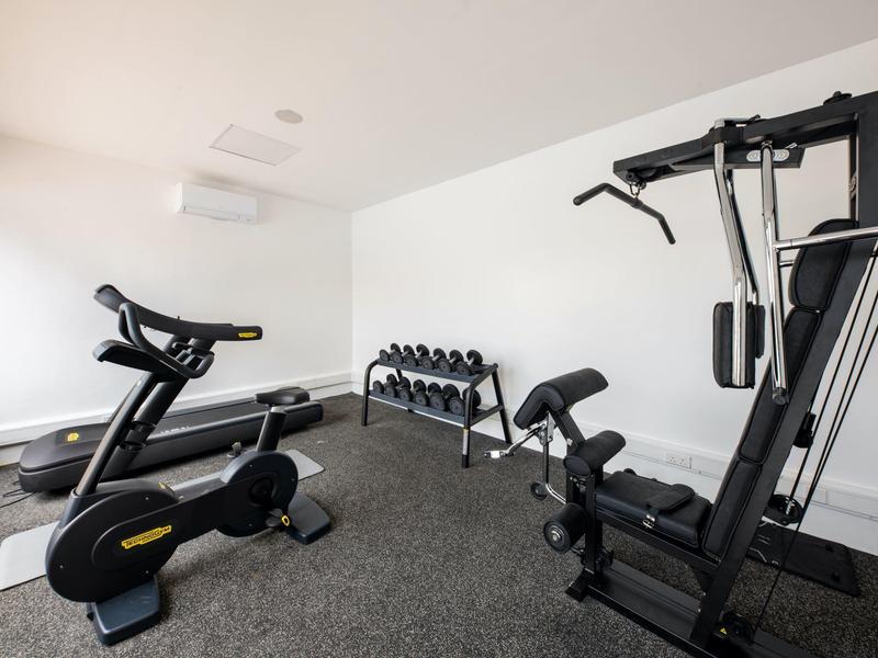 Habitación de gimnasio con equipo de ejercicio, incluyendo bicicleta estática, pesas y máquina multifunción.