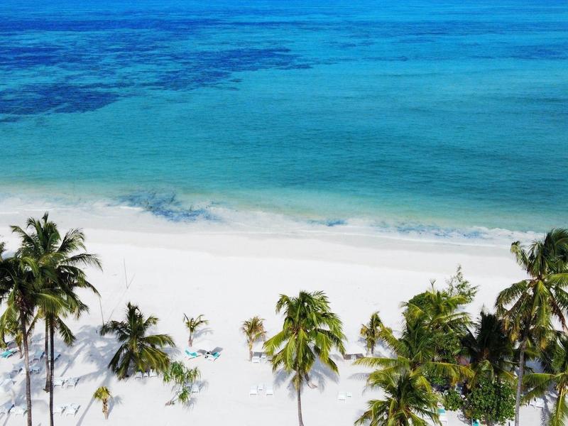 Playa de arena blanca con palmeras y mar azul claro y turquesa en un día soleado.
