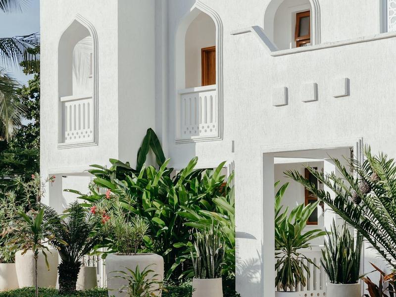 Edificio blanco con ventanas orientales y plantas verdes, típico de un hotel de vacaciones.
