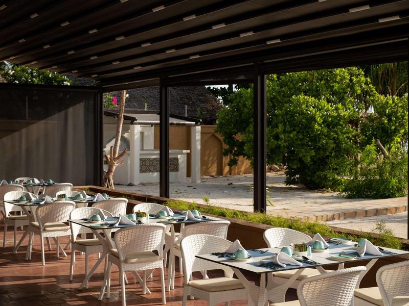 Área exterior destacada de un hotel con mesas preparadas y sillas blancas bajo una estructura cubierta.