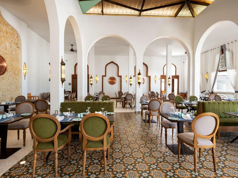 Restaurante elegante de hotel con sillas verdes, suelo de azulejos coloridos y arcos altos redondeados.