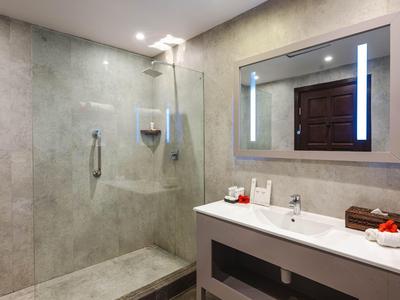 Modernes Badezimmer mit hellgraßer Dusche und Waschbecken, großem beleuchtetem Spiegel, minimalistischer Einrichtung.