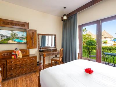 Helles Schlafzimmer mit Holzmöbeln, weißem Bett, Balkon und Blick auf tropischen Garten.