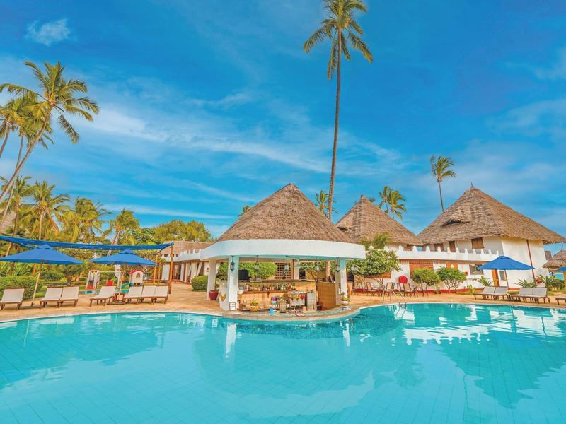 Tropisch zwembad met een swim-up bar, palmbomen en ligstoelen onder een blauwe lucht.