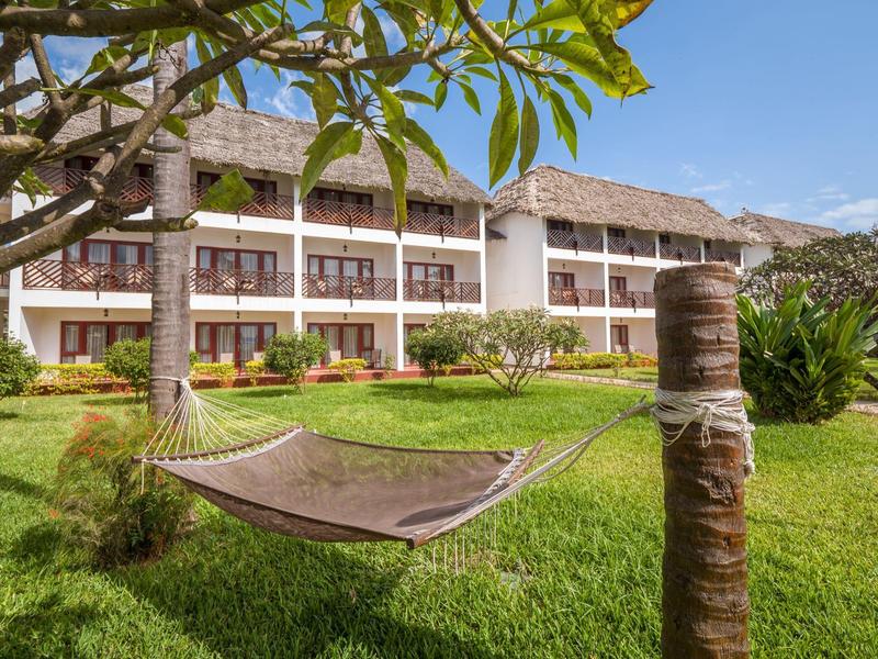 Hangmat in een tuin voor een tweeverdiepingen tellend hotelgebouw met rieten dak.