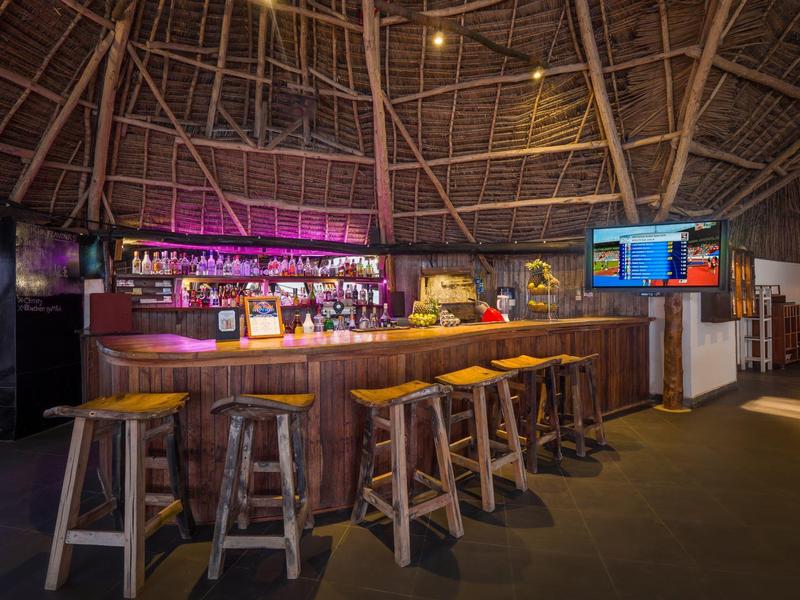 Bar met houten toonbank en krukken onder een hoge, open houten constructie.