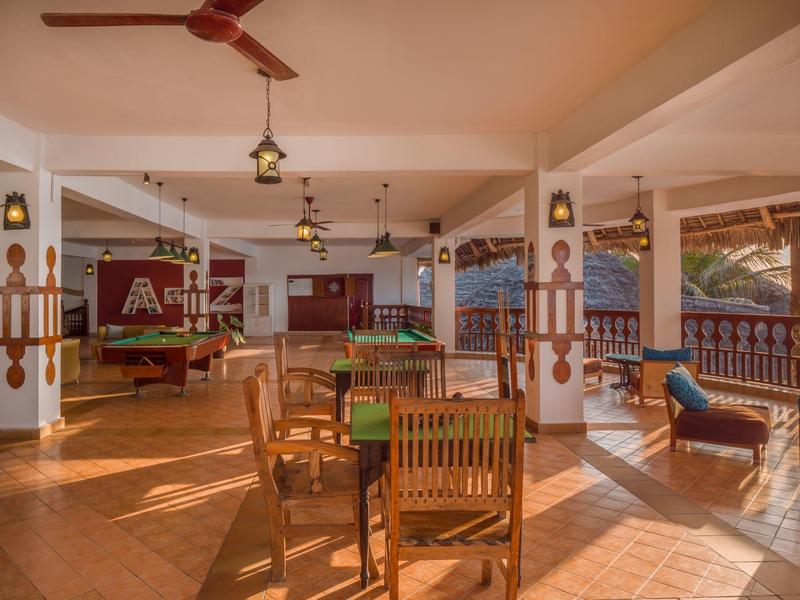 Open lounge met tafels, stoelen en plafondventilator in een hotel.