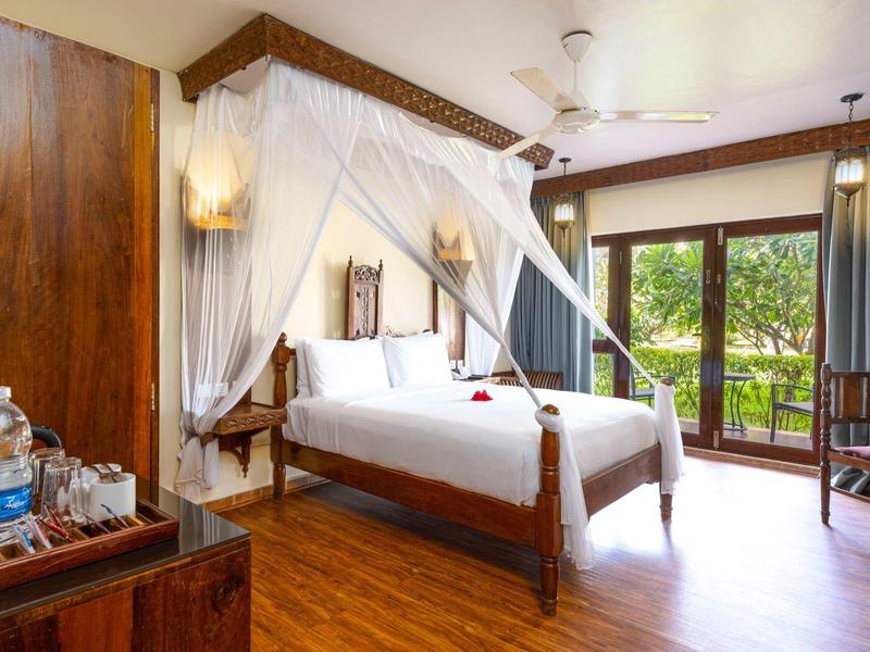 Lichte hotelkamer met hemelbed en uitzicht op groene bomen.