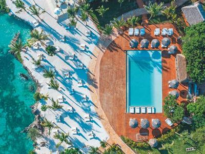 Widok z lotu ptaka na hotel z niebieskim basenem otoczonym palmami i parasolami.