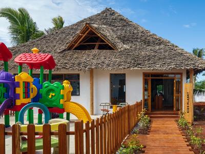 Bungalow z dachem z trzciny i kolorowym placem zabaw przed hotelem w tropikalnym otoczeniu.
