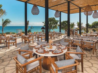 Otwarta restauracja z drewnianymi meblami i widokiem na morze w słoneczny dzień.