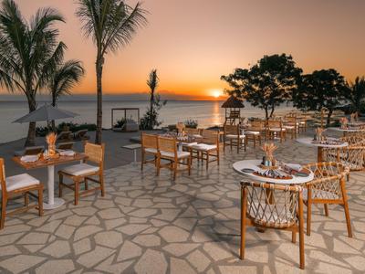 Otwarta restauracja na plaży z drewnianymi stołami i krzesłami o zachodzie słońca.