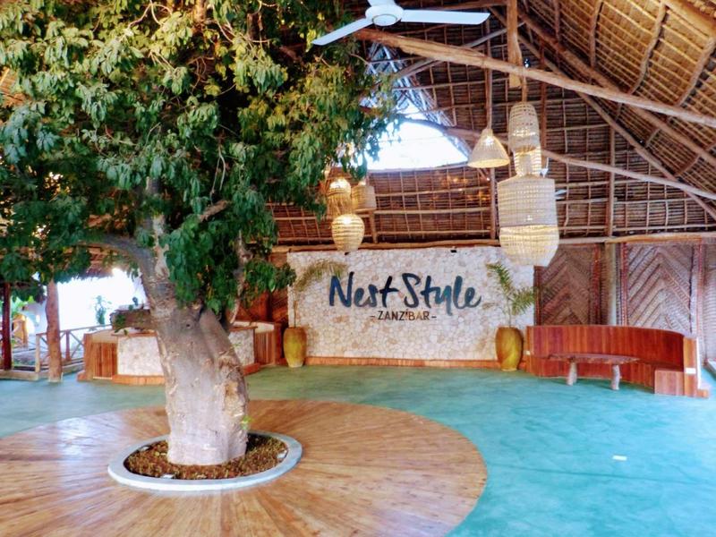 Ampia area dell'hotel luminosa con un albero al centro e una parete con la scritta Neit Style.