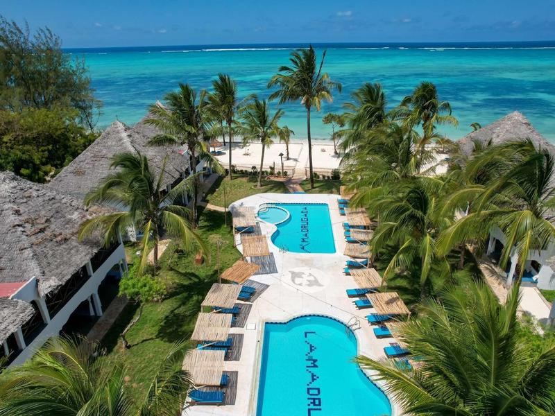 Vista di resort tropicale con piscina, palme e spiaggia sul mare turchese.