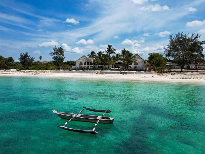 Acqua turchese limpida con una piccola imbarcazione davanti a una spiaggia di sabbia bianca e alberi tropicali.