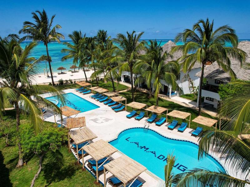 Piscina dell'hotel con lettini e palme sotto un cielo blu vicino alla spiaggia.