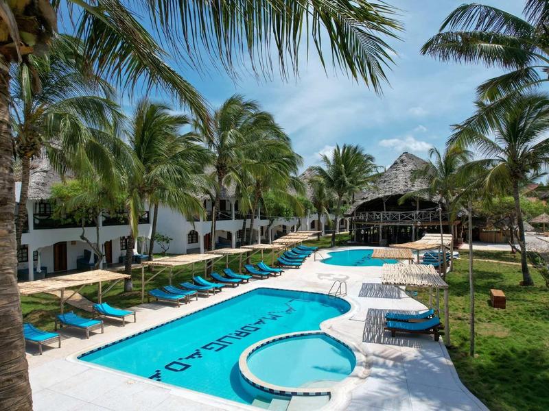 Piscina dell'hotel con lettini sotto palme e ambiente blu in una giornata di sole.