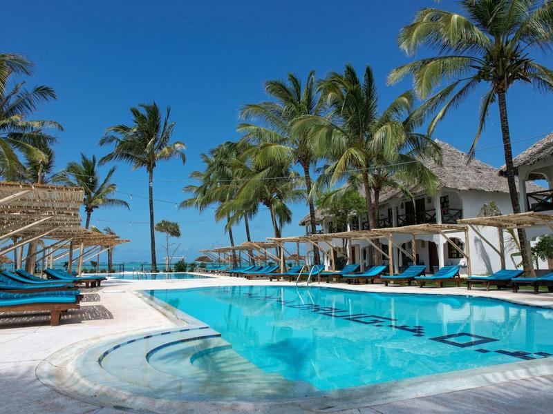 Grande piscina dell'hotel con palme e lettini sotto un cielo azzurro.