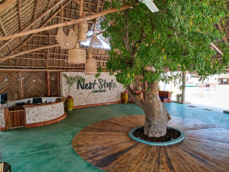 Area aperta con pavimento verde, albero al centro e scrivania della reception sullo sfondo.