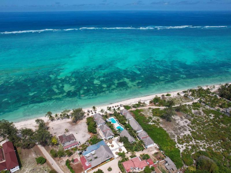 Veduta aerea di una spiaggia con acqua turchese limpida e edifici adiacenti.