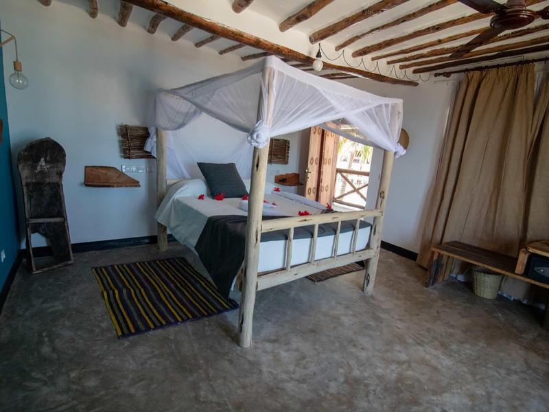 Camera da letto con letto a baldacchino, finestra con tende e travi di legno rustiche sul soffitto.