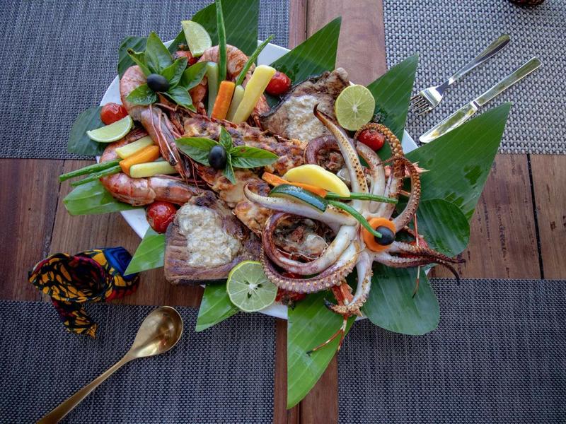 Piatto con frutti di mare grigliati, gamberi e verdure fresche su foglie di banana.