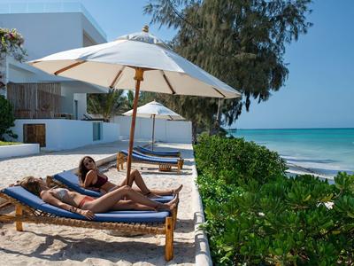 Due persone si rilassano su lettini con ombrelloni vicino a un hotel sulla spiaggia.