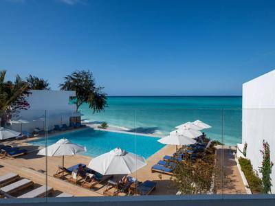 Espace piscine moderne avec chaises longues et parasols blancs au bord de la mer sous un ciel bleu clair.