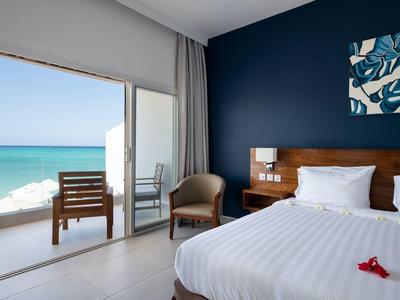 Camera d'hotel moderna con letto matrimoniale, vista mare e terrazza con sedie.