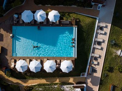 Vue aérienne d'une piscine rectangulaire avec des transats et des parasols à côté d'un bâtiment.