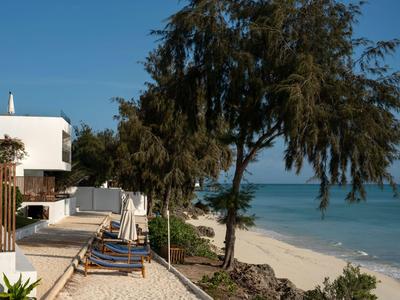 Hôtel en bord de mer avec chaises longues, arbres et vue sur l'océan par ciel clair.