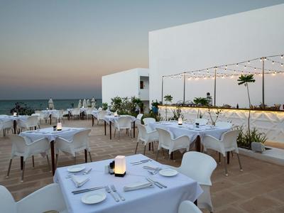 Ristorante all'aperto elegante con tavoli e sedie bianchi al tramonto vicino al mare.