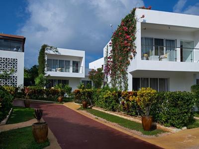 Edifici moderni bianchi di un hotel con balconi e giardino curato sotto un cielo blu.