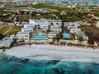 Vista aerea di un resort con edifici bianchi, piscine e spiaggia sabbiosa vicino al mare turchese.