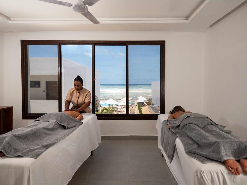 Due persone si rilassano su lettini da massaggio con vista sul mare attraverso una grande finestra.