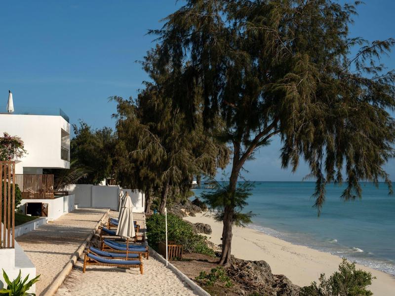 Resort sulla spiaggia con lettini, alberi e vista sull'oceano sotto un cielo sereno.