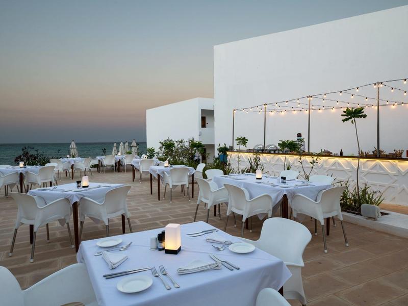 Ristorante all'aperto elegante con tavoli e sedie bianchi al tramonto vicino al mare.