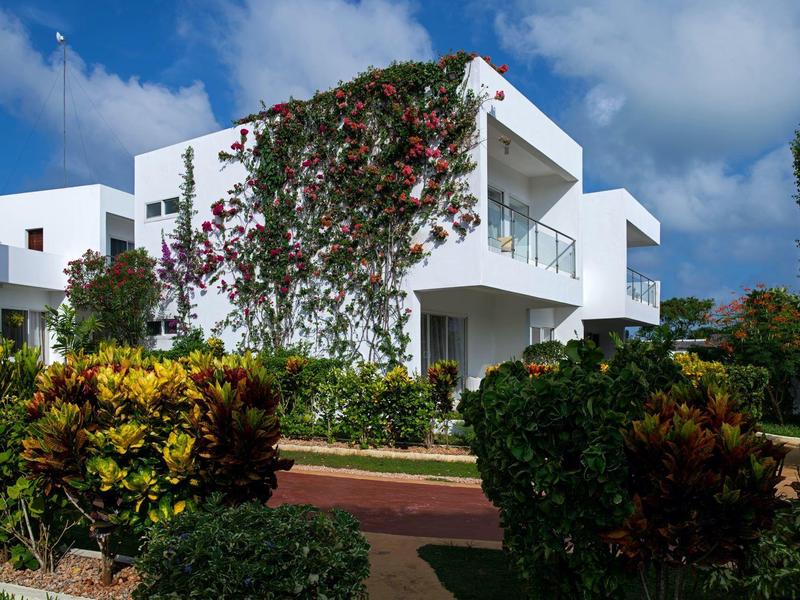Edificio di un hotel bianco moderno con balconi circondato da giardino verde rigoglioso e piante in fiore.