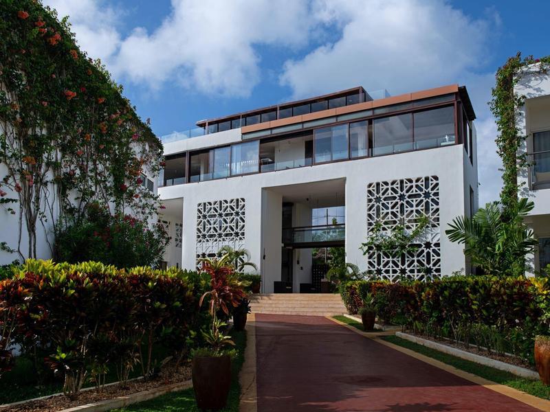 Edificio alberghiero moderno con facciata bianca, piante e cielo azzurro limpido.