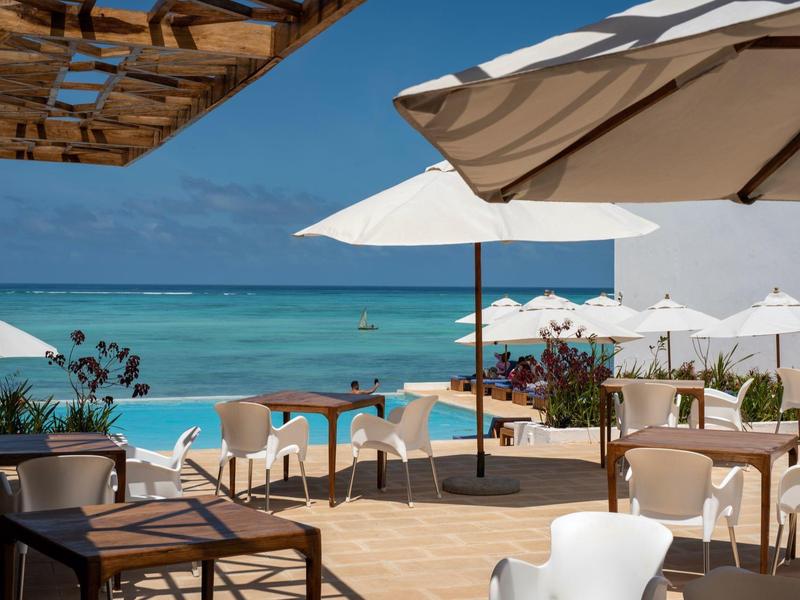 Terrazza con tavoli, sedie e ombrelloni con vista sul mare e il cielo blu.