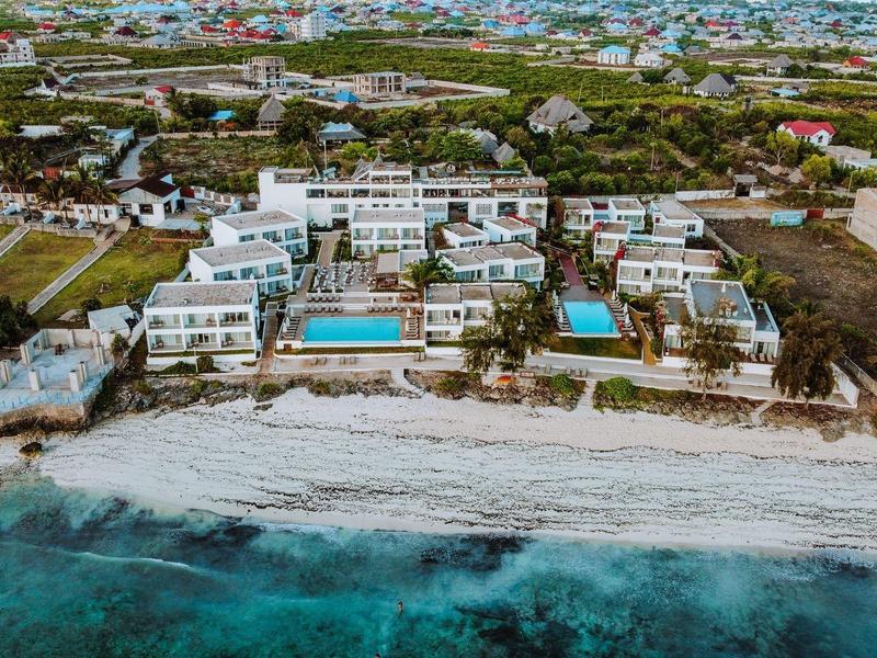Vista aerea di un resort con edifici bianchi, piscine e spiaggia sabbiosa vicino al mare turchese.