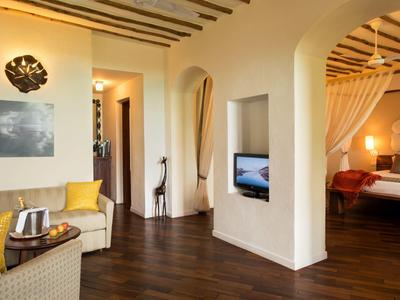 Heller Wohnraum mit dunklem Holzboden, Sofa, gelben Kissen, Fernseher und Schlafzimmer mit Baldachinbett.
