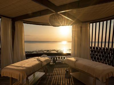 Zwei Massageliegen in einem Holzpavillon mit offenem Blick auf den Sonnenuntergang am Meer.