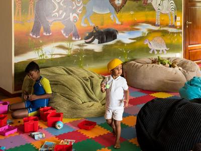 Kinder spielen in einem bunten Raum mit Tierwandbild, großen Sitzsäcken und Spielzeug auf dem Boden.