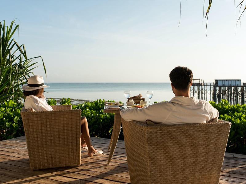Deux personnes sont assises sur une terrasse avec vue sur la mer sous un ciel clair.