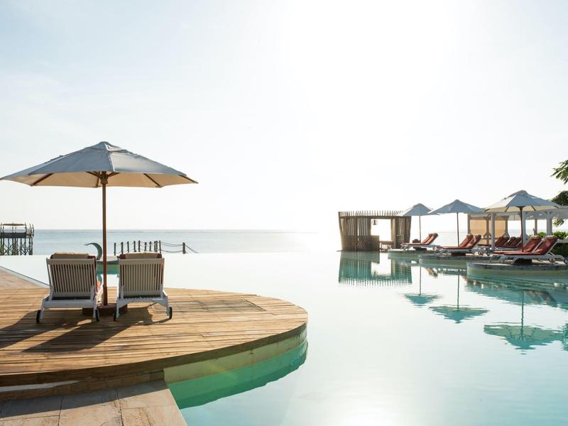Piscine moderne avec transats et parasols face à la mer par une journée ensoleillée