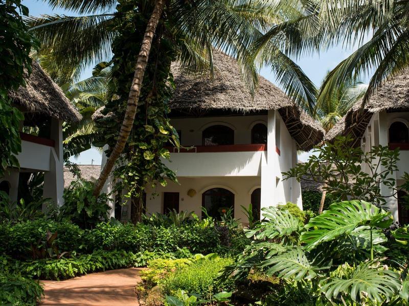 Bungalows au toit de chaume entourés de végétation tropicale et de palmiers sur le terrain de l'hôtel.